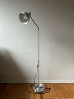 Full view of silver IKEA floor lamp standing on wood floor