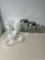 Group view showing three glass jars with two metal lids and stacks of clear plastic cups and containers
