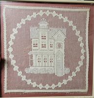 Front view of framed crochet lace panel showing house motif and border