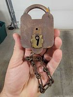 Front view of rusted padlock showing brass keyhole plate and attached chain