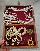 Open wooden jewelry box showing braided bead necklaces in lid section and assorted jewelry in tray