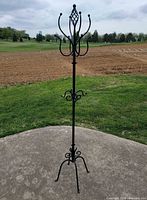 Full view of black wrought iron coat tree with decorative scrolls and hooks