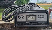 Front view showing model number, dual-rate 6/2 amp labeling, analog meter, and attached cables