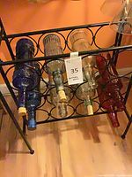 Rack holding eight embossed glass bottles in clear, blue and amber-red glass, most with cork stoppers