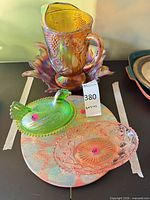 Overview of four visible carnival glass pieces: hen on nest, pitcher, underplate and pink oval dish