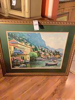 Front view of framed coastal village print with green mat and gold ornate frame
