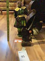 Full view of doll, fish sculpture, lamp base with measuring tape