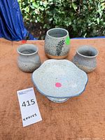 Four pottery pieces arranged: tall vase, two small cups, pedestal bowl