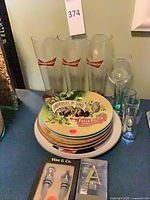 Lot overview: 3 Budweiser glasses, stack of advertising plates, boxed wine stoppers, monogram stopper, additional glassware