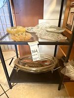 Shelf view showing amber plates, clear tray and oval platter in metal stand