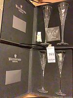 Two open Waterford presentation boxes each holding two crystal champagne flutes with paperwork