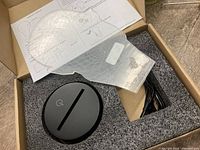 Lamp components in foam insert: acrylic head panel, black LED base, USB cable, instructions