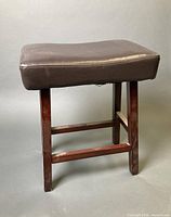 Full view of wooden stool with dark brown faux leather seat