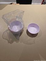 Stack of eight light purple plastic bowls beside partial plastic bag