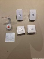 Two rectangular call transmitters, wrist SOS transmitter sealed in plastic, two boxed components and manual displayed