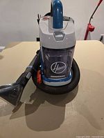 Front view showing Hoover PowerDash logo, clear tank, hose and nozzle attachment