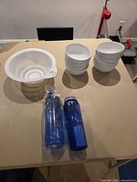 Lot overview showing stacked bowls, colander, and two wrapped bottles