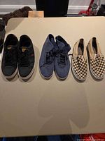 Three pairs of shoes laid out: black Levi Strauss, blue Vans OTW, tan checkerboard Vans Slip-On
