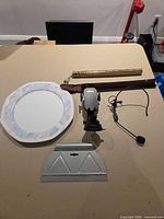 All five items laid out on table: charger plate, brass coin bank with sleeve, phone mount, headset, trowel