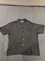 Full view of black short-sleeve silk shirt laid flat