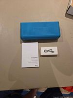 Front view of blue speaker with manual and USB cable
