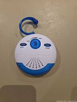front view of round white/blue waterproof shower radio showing controls and hook