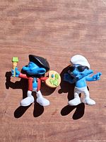 Front view of both Smurf figurines on wooden surface