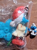 Front of sealed Burger King Smurf figure bag with loose Angel Smurf beside it