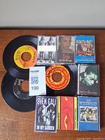 Overview of two 45 RPM singles and seven cassette tapes on tabletop