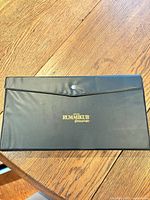 Closed black vinyl case with gold "Deluxe Rummikub pressman" logo