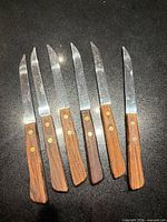 Six wood-handled steak knives laid out blade up