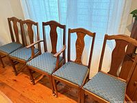 Five oak dining chairs lined up showing overall design and upholstery