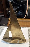 Front view of brass sailboat showing sail and hull