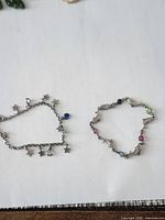 Two silver-plated charm bracelets laid flat on white background