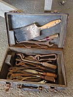 Open metal toolbox with assorted pliers, wrenches and paint brush visible