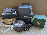 Group view of projector, stacked boxed reels, loose reel, metal tin, NIC box, power cord