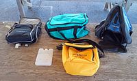 Four items laid out: Transpack backpack, teal duffel, yellow cooler, white ice pack