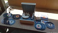 Turntable with case open, power cord, and spread of 45 RPM records