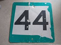 Front view of square Route 44 sign showing white reflective face, green border, black numerals, mounting holes, surface wear