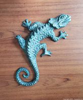 Full view of verdigris green gecko wall sculpture on wood background