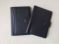 Two closed black leather passport holders showing front embossing and snap tab