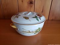 Side view of covered casserole showing fruit motif, gold handle and trim
