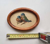 Front view of oval petit point birds embroidery with tape measure for scale