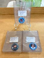 Overall view of three pinback buttons in sleeves on display stands