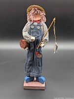 Full view of fisherman figurine on base with rod and basket