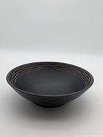 Angled view of black wooden bowl showing carved exterior and gold-tone inlay