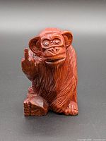 Wooden monkey sculpture raising middle finger, frontal view