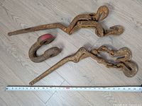 Two lever load binders and one slip hook laid beside measuring tape