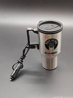 Front view of Bell + Howell Hot N' Go heated travel mug showing logo, lid, handle and attached 12V car adapter cord