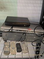 Three video components stacked with four remotes on shelf